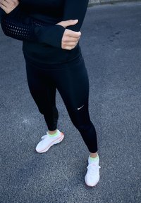 Sorte atletiske leggings med teksturerede sidelapper, parret med hvide sneakers med neonlys og et reflekterende logo.