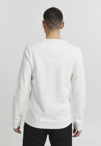 Felpa bianca a girocollo con maniche lunghe, tessuto morbido, polsini e orlo a costine, design minimalista, senza loghi o motivi visibili.