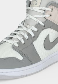 Γκρι και λευκό Nike Air sneaker με πάνελ από δίχτυ και δέρμα, λευκά κορδόνια και έντονο λογότυπο Nike στο πλευρό.