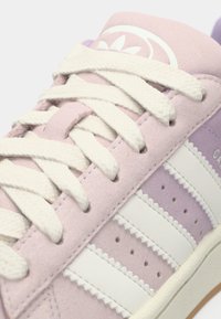 Light pink suede sneakers with white leather stripes, featuring textured laces and subtle detailing on the tongue. Flat rubber sole.