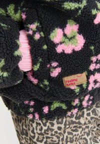 Čierna chundelatá bunda s zelenými a ružovými kvetinovými vzormi, so štítkom "Cítim sa šťastne", na béžovom a čiernom vzore leopardu.