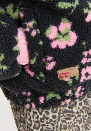 Czarna futrzasta kurtka z zielonymi i różowymi kwiatowymi wzorami, z metką "Czuję się szczęśliwy", na beżowym i czarnym materiale w leopardzie.