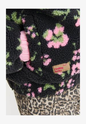 Czarna futrzasta kurtka z zielonymi i różowymi kwiatowymi wzorami, z metką "Czuję się szczęśliwy", na beżowym i czarnym materiale w leopardzie.