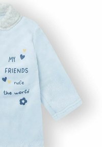 Bata de forro polar azul claro con un cuello suave. Presenta texto impreso en azul oscuro y amarillo, incluyendo corazones y un patrón de flores.