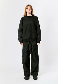 Sudadera negra con patrón texturizado y logo "MWM" en la parte delantera. Combinada con pantalones holgados a juego y calzado negro texturizado.