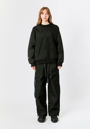 Sudadera negra con patrón texturizado y logo "MWM" en la parte delantera. Combinada con pantalones holgados a juego y calzado negro texturizado.