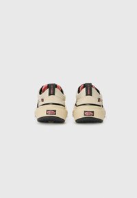 Kremfargede sneakers med en strukturert gummisåle, svarte detaljer og rød fôr. Har en trekkstang og et distinkt logo på hælen.
