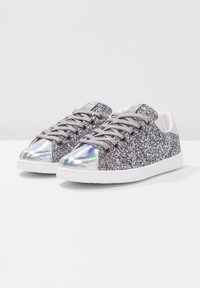 Baskets argentées scintillantes avec un capuchon de pied lisse irisé, des lacets gris et des semelles blanches, présentant un design supérieur en paillettes texturé.