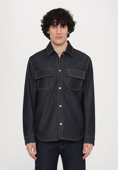 Cămașă din denim închis, cu închidere cu nasturi în față, două buzunare pe piept, cusături de culoare galben contrastantă și un design clasic al gulerului.