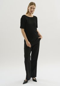 Schwarzes, strukturiertes Oberteil mit kurzen Ärmeln, kombiniert mit schwarzen, geraden Hosen und spitzen Schuhen. Einfaches Design, ohne Muster oder Akzente.