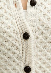 Dziewiądza kremowa kardigana z wypukłym wzorem, czterema ciemnobrązowymi guzikami i otwartym dekoltem, ukazująca misterny rzemiosło.