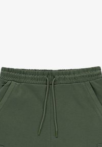 Donkergroene sweatpants hebben een elastische tailleband met een trekkoord, zijzakken en een zachte, gladde stoftextuur.