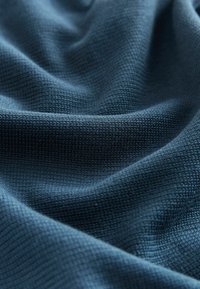 Prim-plan cu material texturat albastru închis, cu un model mic țesut și cute moi care creează umbre și profunzime.