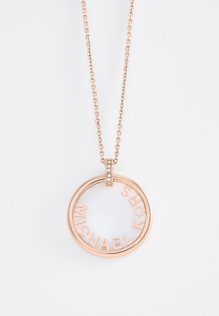 Pendentif en or rose sur une chaîne, présentant un design circulaire, gravé avec "MICHAEL KORS" et rehaussé de petits diamants clairs.