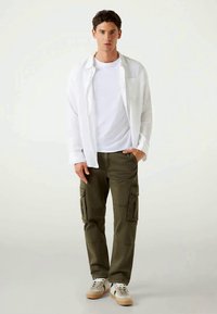 Camisa de algodão branca com botões, t-shirt branca lisa, calças cargo verde-oliva com bolsos, ténis bege com detalhes em verde e preto.