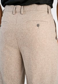 Pantalones de lana color beige claro con una superficie texturizada, que presentan una cinturilla, un bolsillo trasero y un detalle de botón.