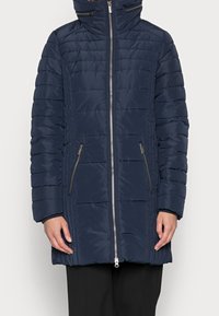 Abrigo tipo puffer de color navy con cierre frontal, cuello alto y bolsillos laterales. Presenta costuras horizontales y un acabado suave y brillante.