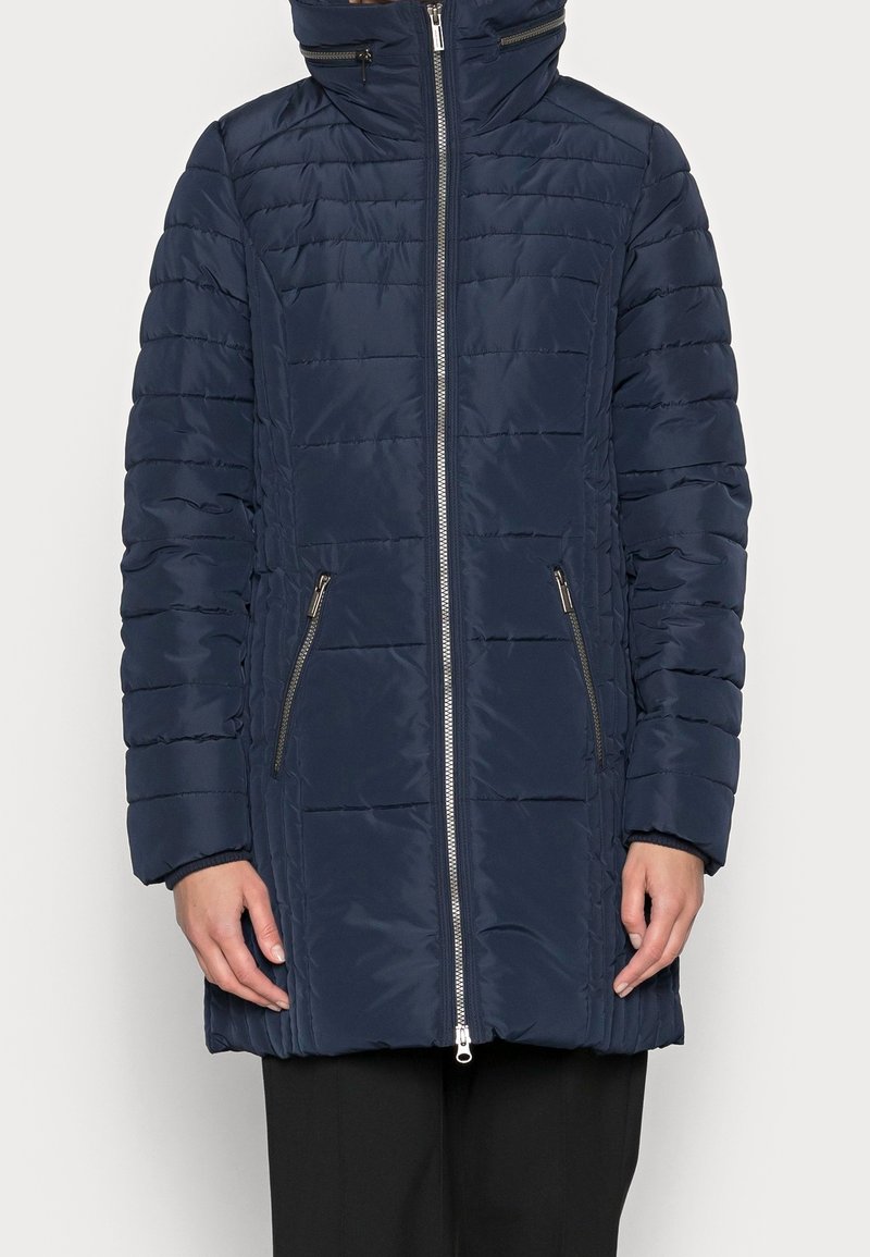 Abrigo tipo puffer de color navy con cierre frontal, cuello alto y bolsillos laterales. Presenta costuras horizontales y un acabado suave y brillante.