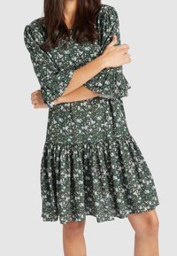 Vestido floral verde con mangas cortas con volantes, una cintura fruncida y una falda acampanada. Presenta patrones de flores blancas y rosas sobre un fondo oscuro.