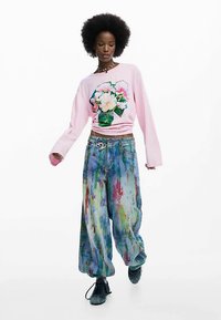 Roze sweatshirt met bloemenprint, gecombineerd met wijde jeans met een kleurrijk spettereffect. Zwarte sneakers maken de outfit compleet.