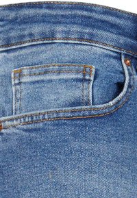 Jeans de denim azul con una cinturilla curvada, un pequeño bolsillo trasero y costuras naranjas en los bordes.