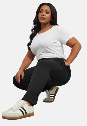 Un jogging noir avec des poches latérales associé à un t-shirt blanc ajusté et des baskets beiges avec des rayures noires et une semelle marron.