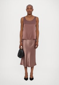 Brown satin sleeveless top paired with a matching midi skirt. Black handbag in hand, black pointed-toe shoes. Smooth texture, soft sheen.