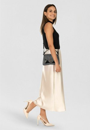 Top nero a coste senza maniche, gonna midi in satin crema, tacchi alti color tan e borsa nera testurizzata con dettaglio logo.