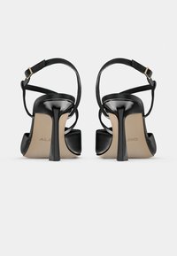 Sandales à talons hauts en cuir verni noir avec une fine bride autour de la cheville et un bout carré ouvert, dotées d'un élégant talon aiguilles et d'une semelle intérieure beige.