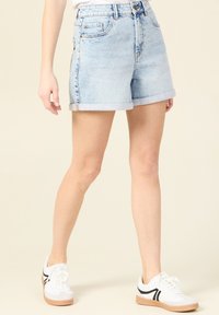 Vaaleansiniset farkkushortsit, joiden lahkeet on käännetty, edessä ja takana taskut. Yhdistetty valkoisiin tennareihin ja yksinkertaiseen valkoiseen toppiin.