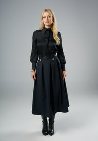 Czarna satynowa bluzka z wysokim kołnierzem i bufiastymi rękawami, w połączeniu z ciemną, plisowaną spódnicą z złotymi guzikami i paskiem. Czarne botki za kostkę.