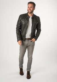 Schwarze Lederjacke mit Schulterakzenten, zwei Reißverschlusstaschen und einer glatten Textur, getragen über einem weißen T-Shirt und grauen Jeans. Braune Stiefel.
