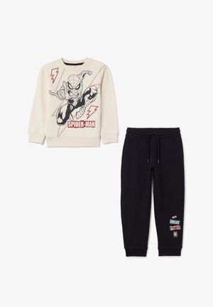 Felpa beige chiaro con grafica di Spider-Man, abbinata a pantaloni della tuta neri con accenti di testo rossi e blu. Tessuto morbido in misto cotone.