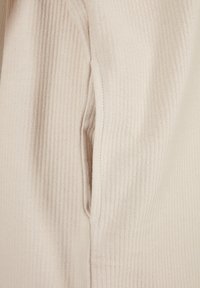 Tissu beige côtelé avec une couture latérale verticale et une ouverture de poche fendue verticale.