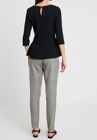 Top peplum nero con maniche a tre quarti, dettaglio a occhiello sul retro; abbinato a pantaloni tailleur a quadri grigi e sandali neri.