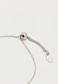 Ρυθμιζόμενο ασημένιο κολιέ αλυσίδας με στρογγυλό κούμπωμα με γλιστρώντας χάντρα και μικρό μενταγιόν με χαραγμένο κύκνο σε λευκό φόντο.