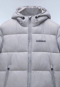 Giacca trapuntata grigia chiara con cappuccio, dotata di scomparti cuciti, tasche laterali con zip e un logo sulla parte sinistra del petto. Texture liscia.