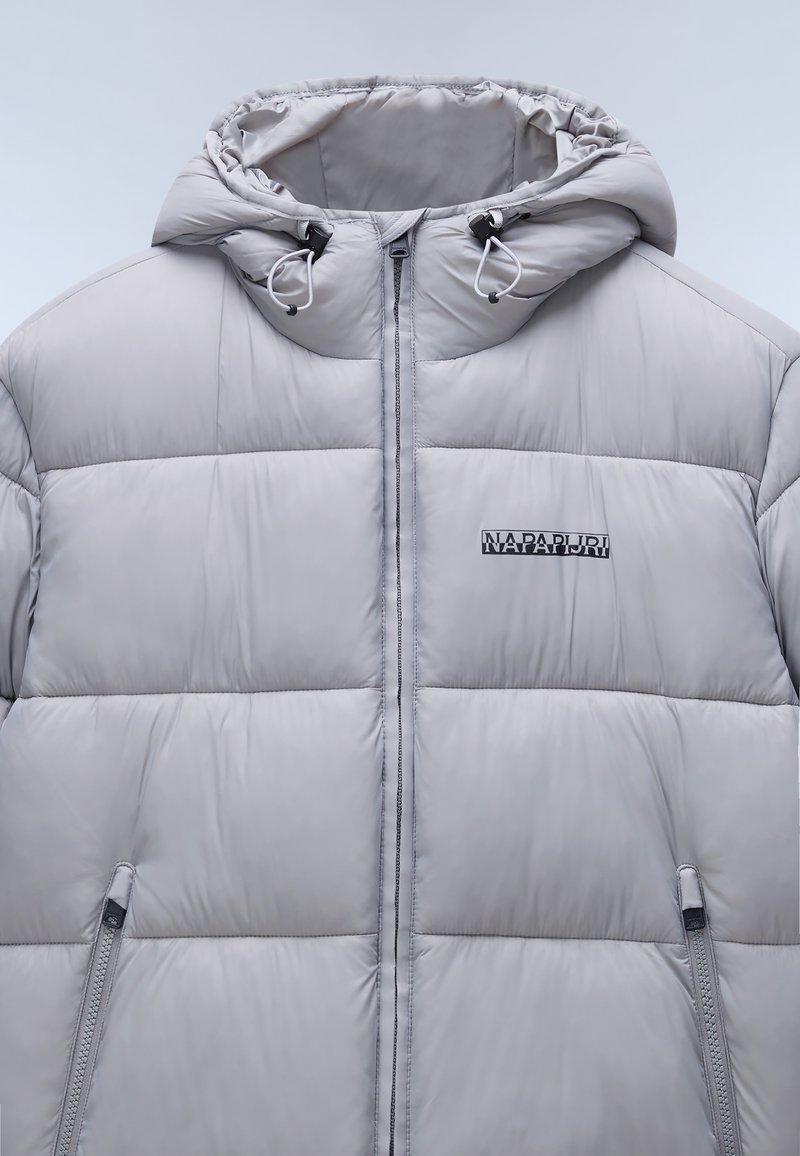 Helle graue Pufferjacke mit Kapuze, die genähte Fächer, Reißverschlusstaschen an den Seiten und ein Logo auf der linken Brustseite aufweist. Glatte Textur.