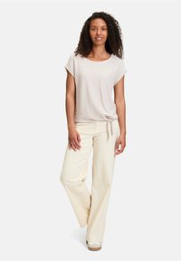 Haut beige clair à manches courtes avec un motif texturé, assorti à un pantalon crème à jambes larges. La tenue comprend un détail de nœud sur le côté du haut.