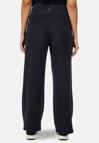 Schwarze weit geschnittene Hosen mit glatter Textur, hohem Bund und Logodetail auf der Rückseite. Sie verfügen über einen lässigen Schnitt bis zu den Knöcheln.