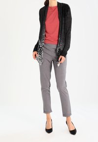 Svart cardigan med vitt mönster vid fållen, i kombination med en röd skjorta. Gråta figursydda byxor och svarta högklackade skor fulländar outfitten.