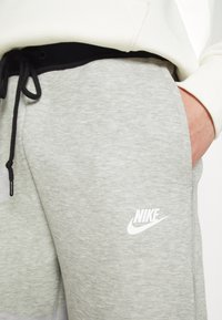 Grå bomullsblandning joggers med svart dragsko, med en vit Nike-logotyp på vänster lår och en slät yta.