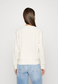 Ljus krämfärgad sweatshirt med rund hals, ribbade ärmslut och nederkant. Tyget verkar mjukt och är parat med ljusblå högmidjade jeans.