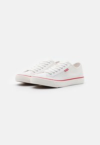 Sneakers in tela bianchi con una striscia rossa e logo, dotati di lacci standard, suole in gomma e design a profilo basso.