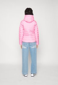 Vaaleanpunainen toppatakki hupulla, jossa tikattu kuviointi ja napakka istuvuus. Yhdistetty vaaleansinisiin leveälahkeisiin farkkuihin ja valkoisiin tennareihin.