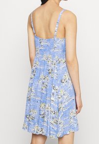 Niebieska sukienka letnia z cienkimi ramiączkami, z nadrukiem palm. Lekka tkanina, dopasowany gorset, rozkloszowany dół i teksturowana powierzchnia.
