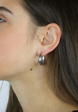 Srebrna kolczyk kołowy prezentowany na płatku ucha, charakteryzujący się gładkim, zaokrąglonym kształtem z wypolerowaną powierzchnią i delikatnym skrętem.