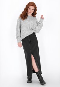 Maglione grigio lavorato a maglia con spalle scese, abbinato a una gonna maxi in denim nera con spacco frontale e stivaletti neri.