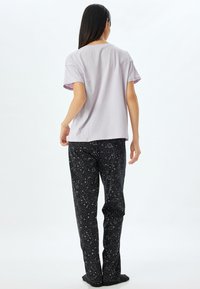 Lichtpaarse, korte mouwen t-shirt gecombineerd met zwarte broek met een wit sterrenpatroon. Casual, losse pasvorm.