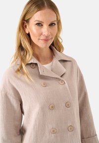 Hellesbeige, doppelt geknöpfter Mantel aus strukturiertem Stoff, mit großen Knöpfen und Reverskragen. Verfügt über eine lockere Passform und lange Ärmel.